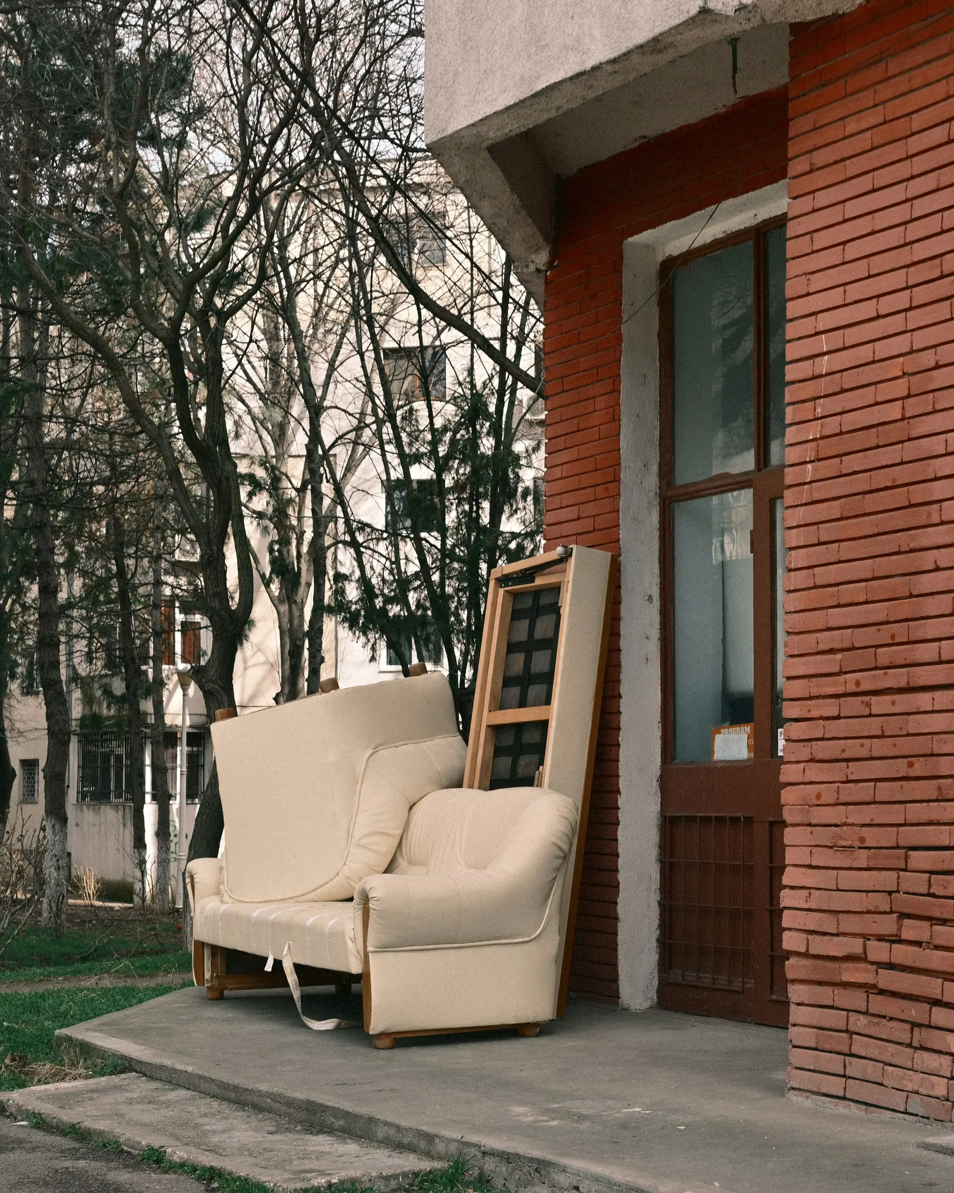 An old armchair and sofa left outside a brick building
